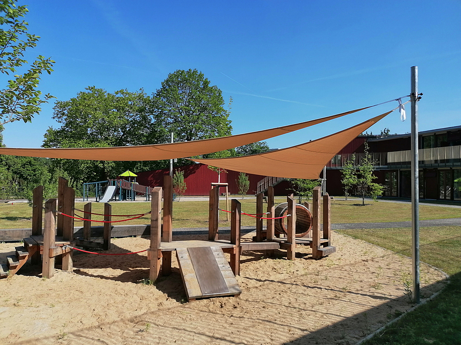 Kleinkinderspielplatz mit Sonnensegeln, Rasen, L-förmiges Gebäude mit Terrasse