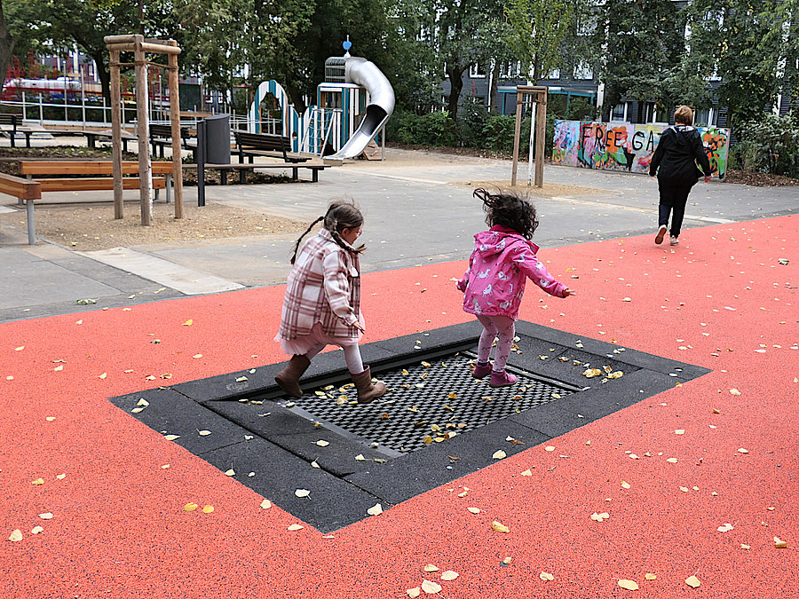 2 Kinder springen auf Bodentrampolin auf rotem Kunststoffboden