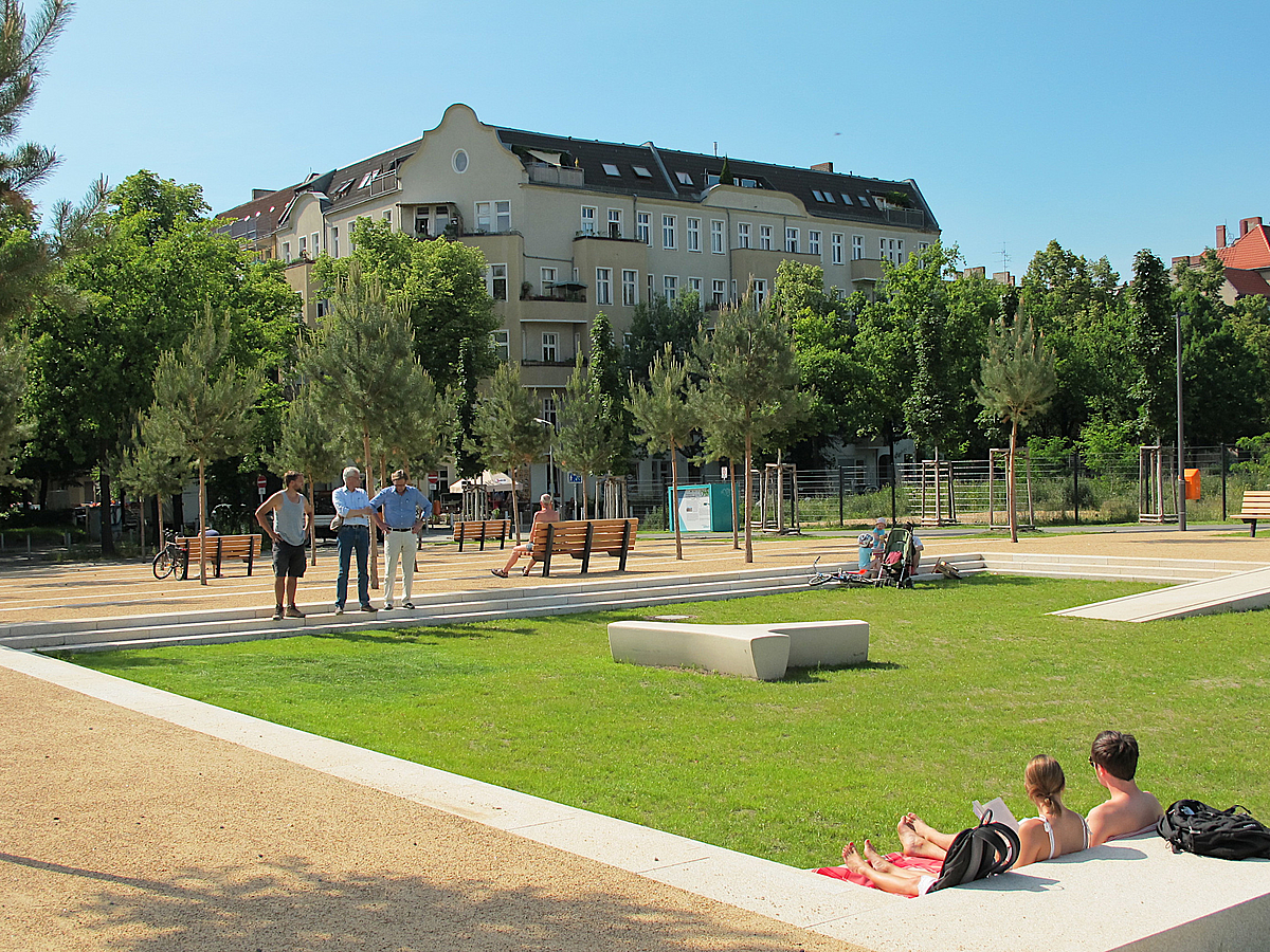 Rasen mit Sonnenbadenden, Beton-Sitzelemente, junge Bäume, Wohnbebauung