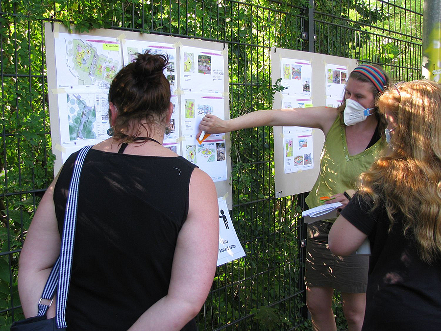 3 Frauen diskutieren am Plakat am Zaun