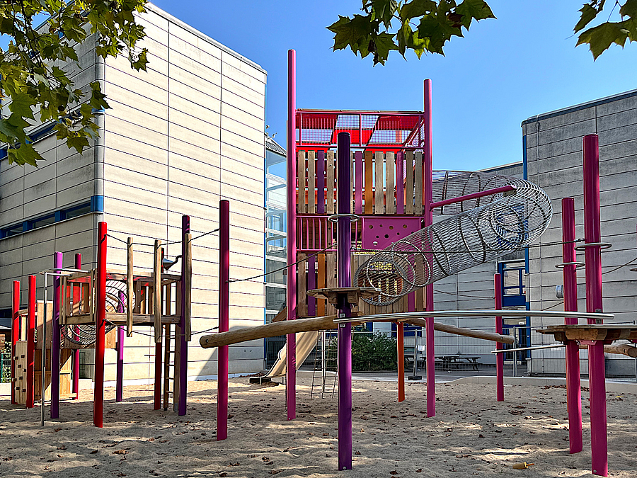Die neue große Kletteranlage auf dem Grundschulhof Großes Klettergerät auf Sandfläche im Hof zwischen modernen Schulbauten