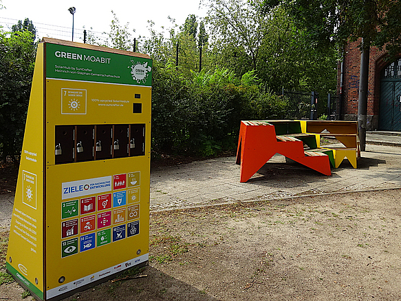 Gelber Aufsteller mit Infografiken, Farbige Sitzmöbel auf Schulhof