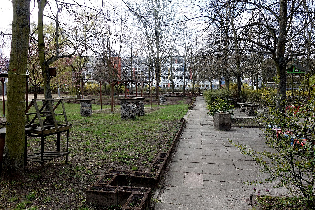 Plattenweg, Stehtische auf Rasen, Bäume im Vorfrühling