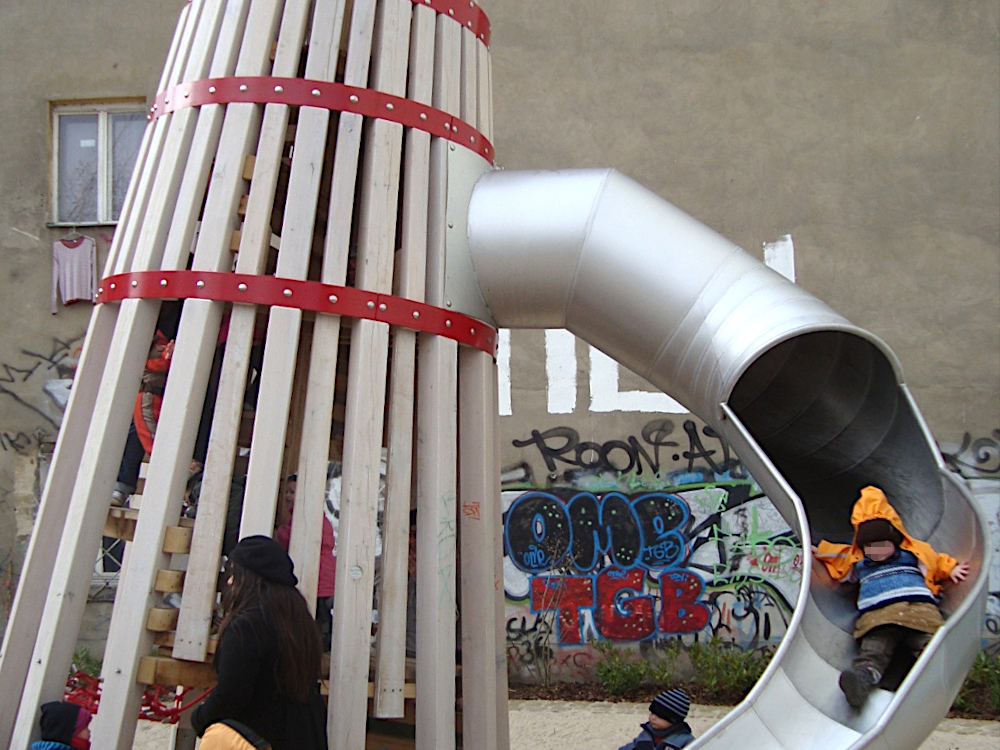 Holzturm mit Rutsche vor Hauswand mit Graffiti