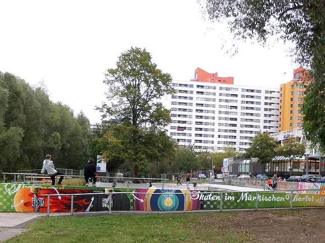 Blick auf Umfassungsmauer mit Graffiti, im Hintergrund Bäume und Hochhäuser